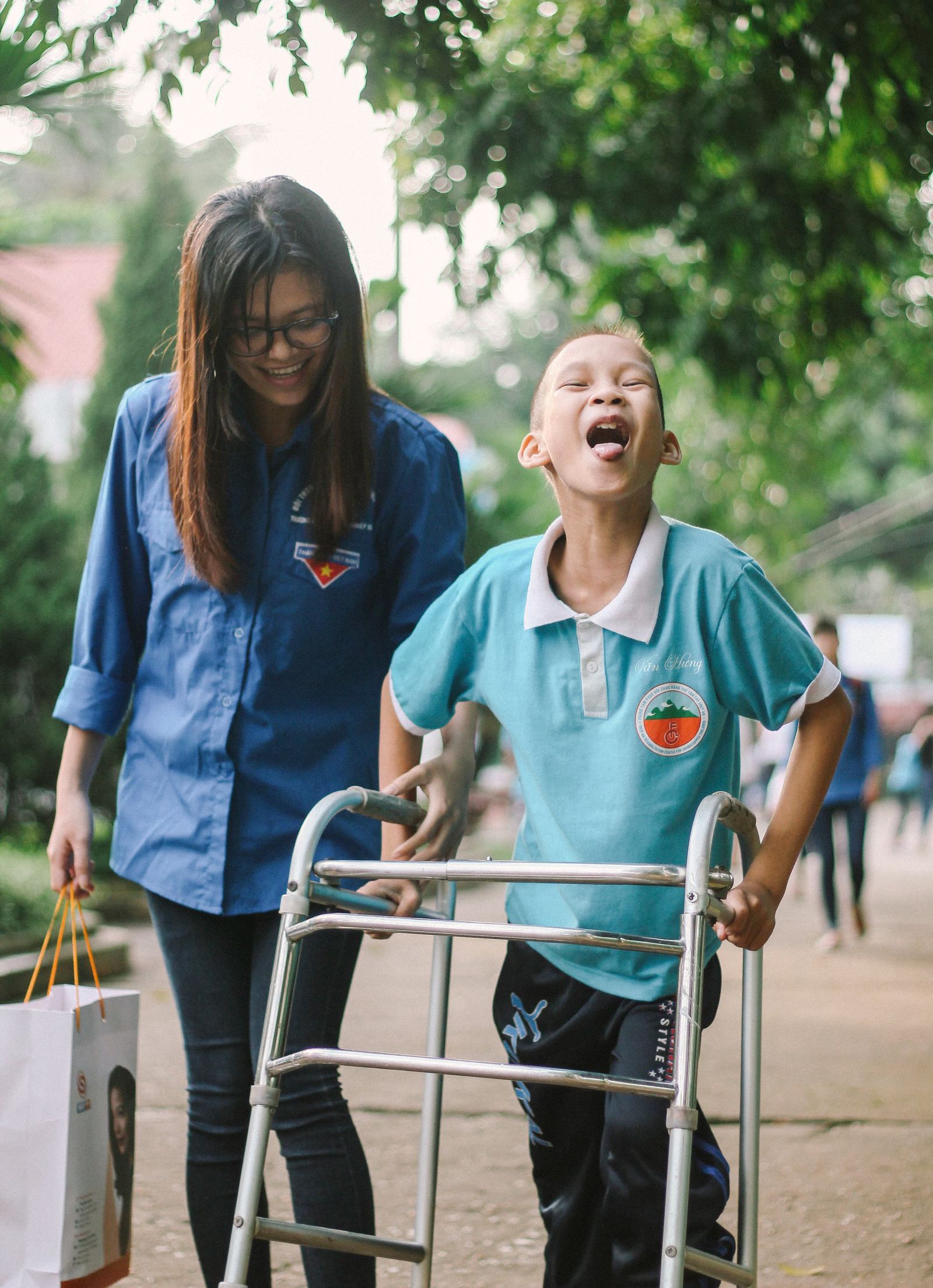 A smiling boy walking with his walker, supported by a caring therapist